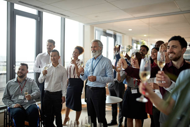 Bearded CEO and multi-ethnic executive team looking away from camera and smiling as they stand with flutes of champagne and prepare for celebratory toast.